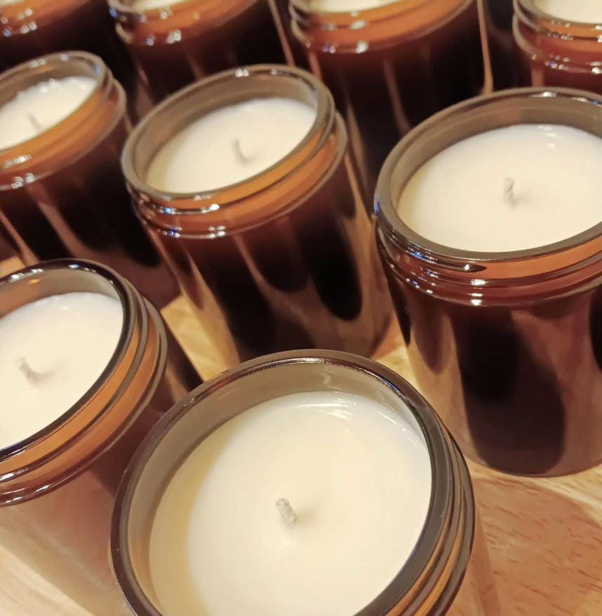 Close-up of several brown glass jars with white candles inside on a wooden surface. Displaying runcorn wax manufacturing method pouring candles