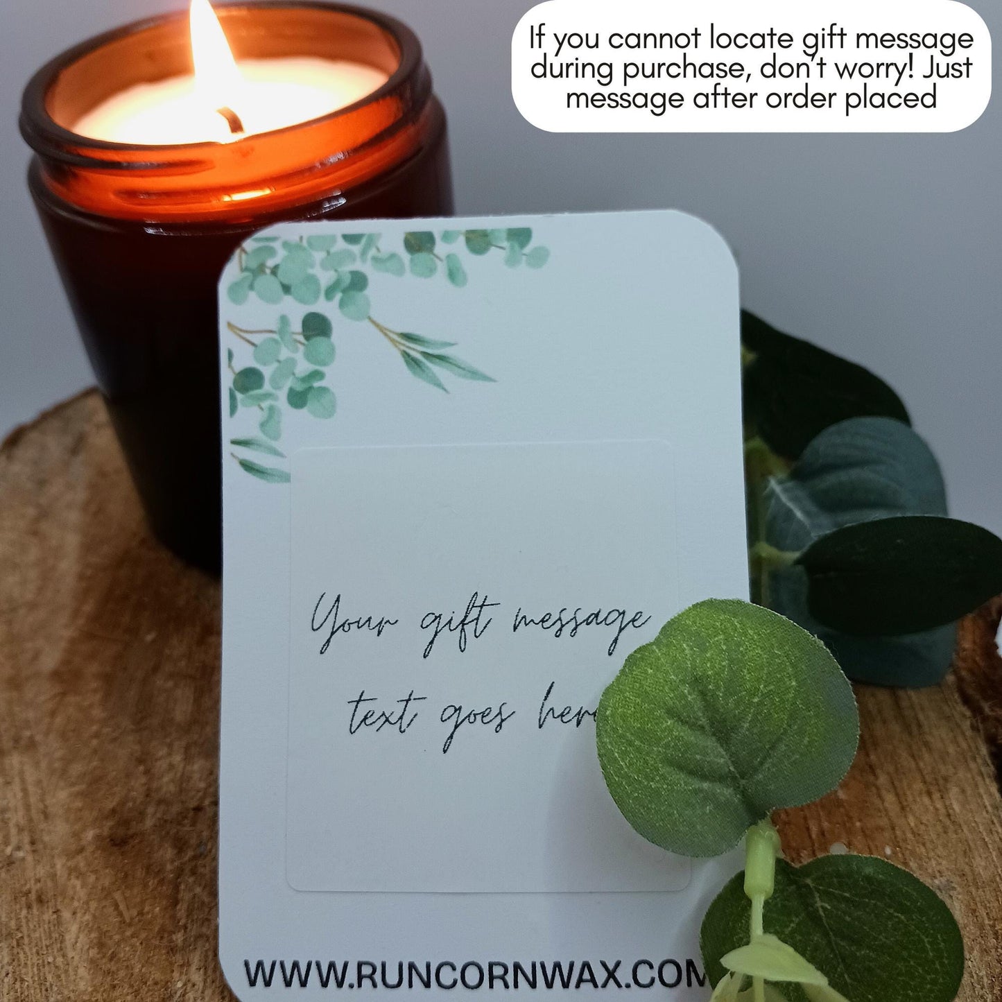 Candle with a decorative card and eucalyptus leaves on a wooden surface