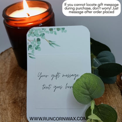 Candle with a decorative card and eucalyptus leaves on a wooden surface
