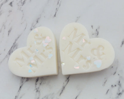Two heart-shaped soap bars with engraved text on a marble surface