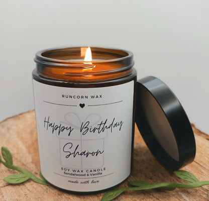 Candle in a jar with a label reading 'Happy Birthday Sharon' on a wooden surface.