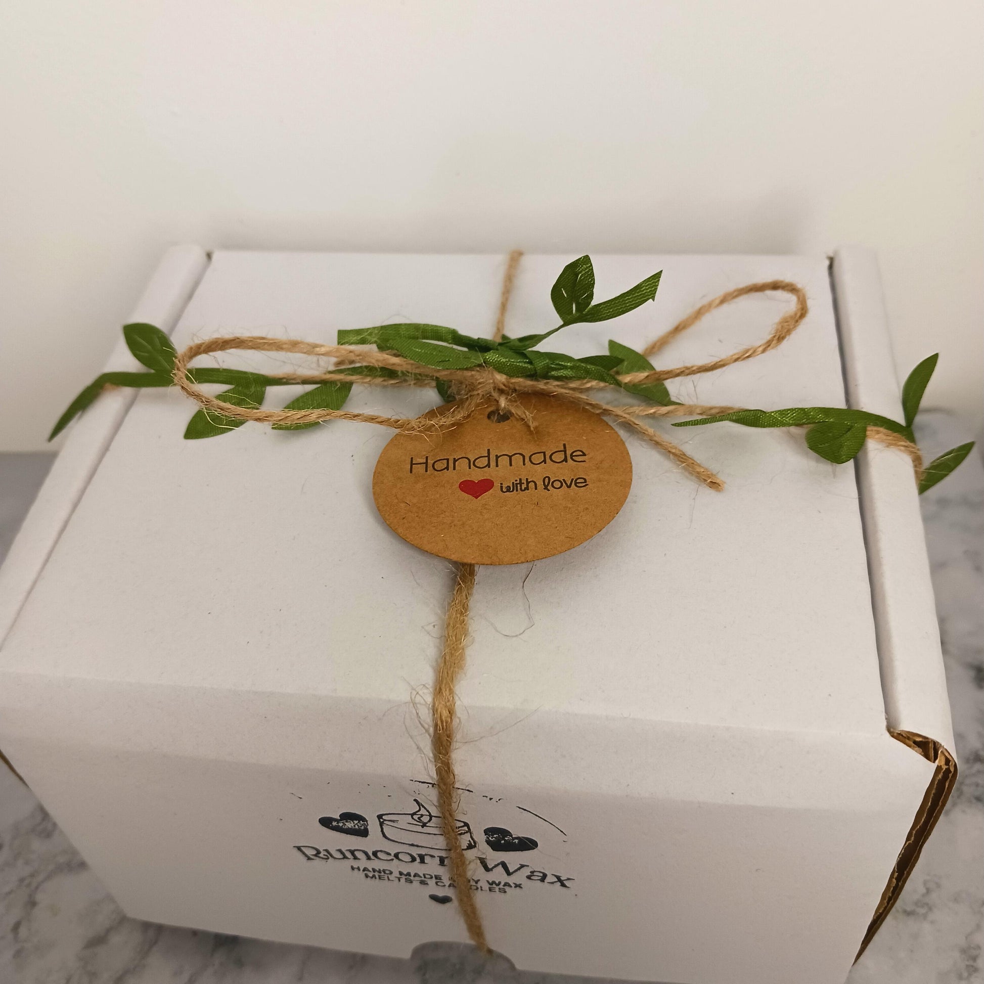 White box with a handmade tag and greenery on a white background