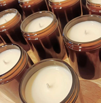 Close-up of several brown glass jars with white candles inside on a wooden surface.