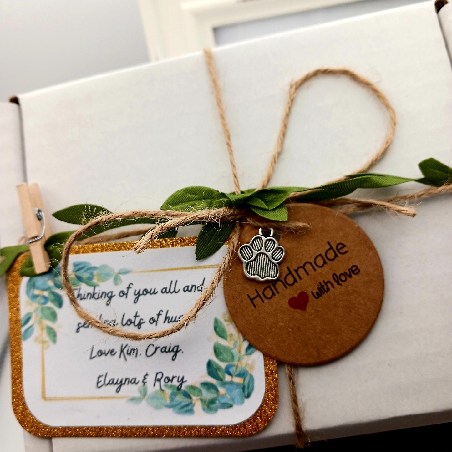 Gift box with a decorative tag and string, featuring a paw print charm and handwritten message.