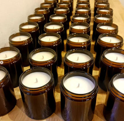 Multiple brown glass jars with white candles on a wooden surface.