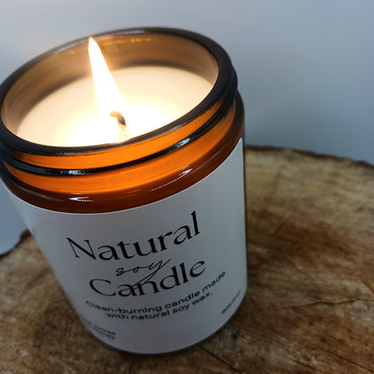 Candle in a jar labeled 'Natural Soy Candle' on a wooden surface.
