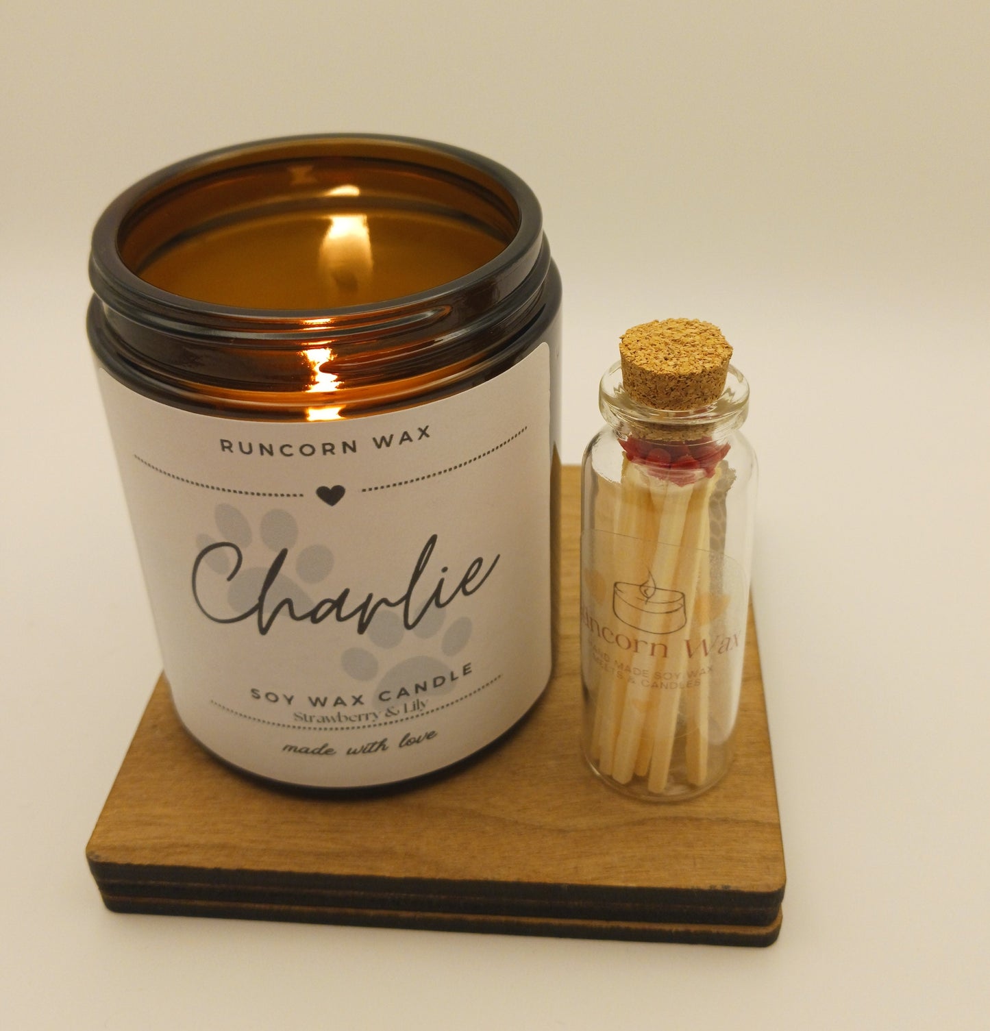 Candle labeled 'Charlie' with a small bottle of matches on a wooden coaster.