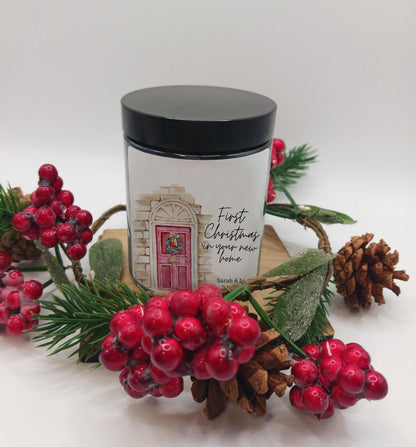 Candle in a amber jarcontainer with a black lid surrounded by festive decorations on a white background
