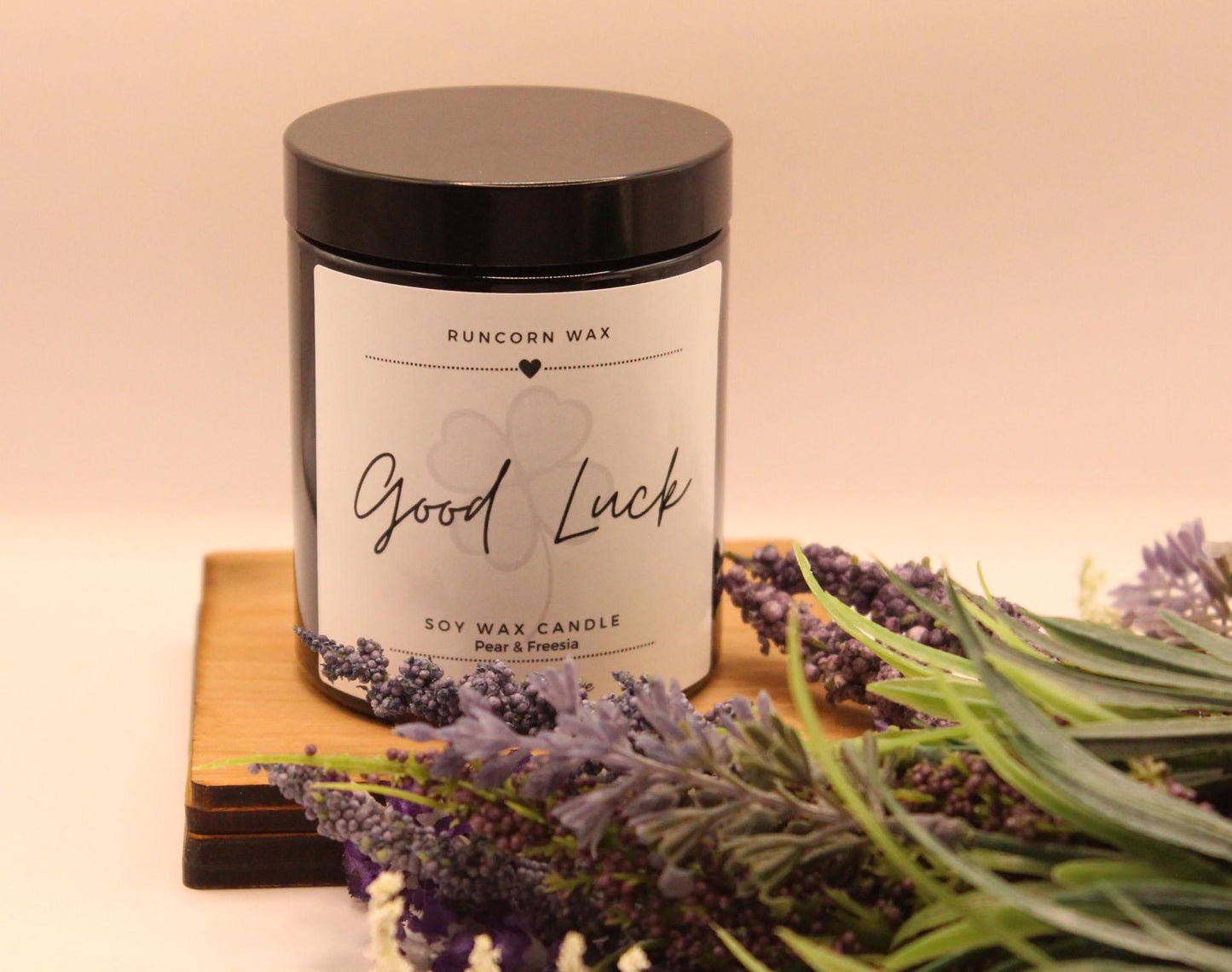 Candle labeled 'Good Luck' with lavender flowers on a wooden board