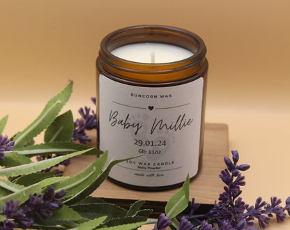 Candle in a glass jar with a label, surrounded by lavender flowers on a wooden surface.