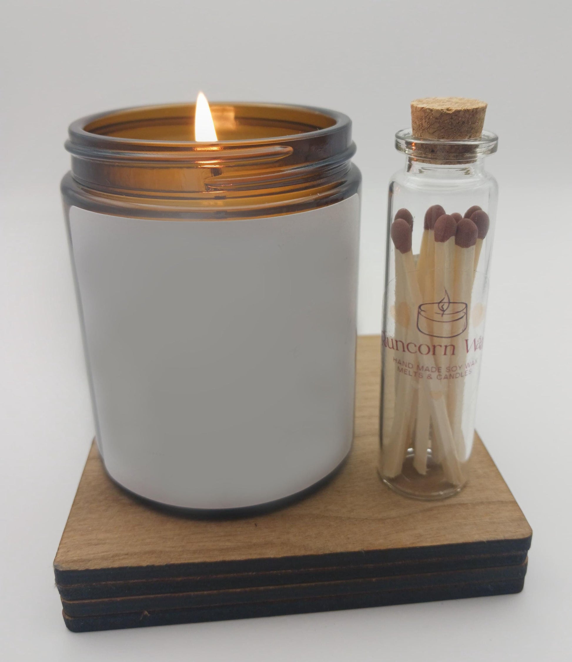 Lit candle in a white jar with matches in a glass bottle on a wooden coaster.