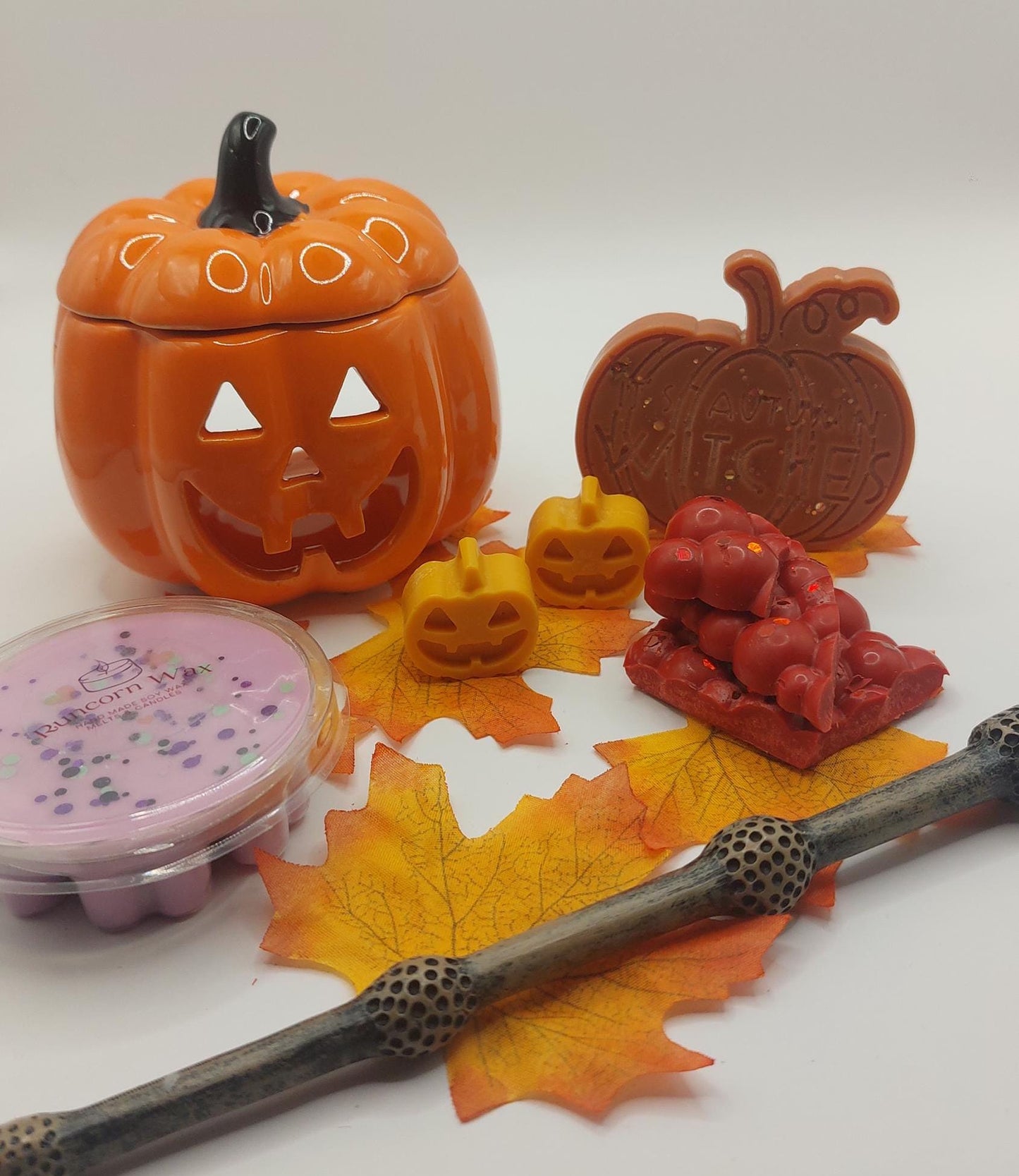 Halloween-themed items including a jack-o'-lantern-shaped container, candles, and decorative elements on a white background.