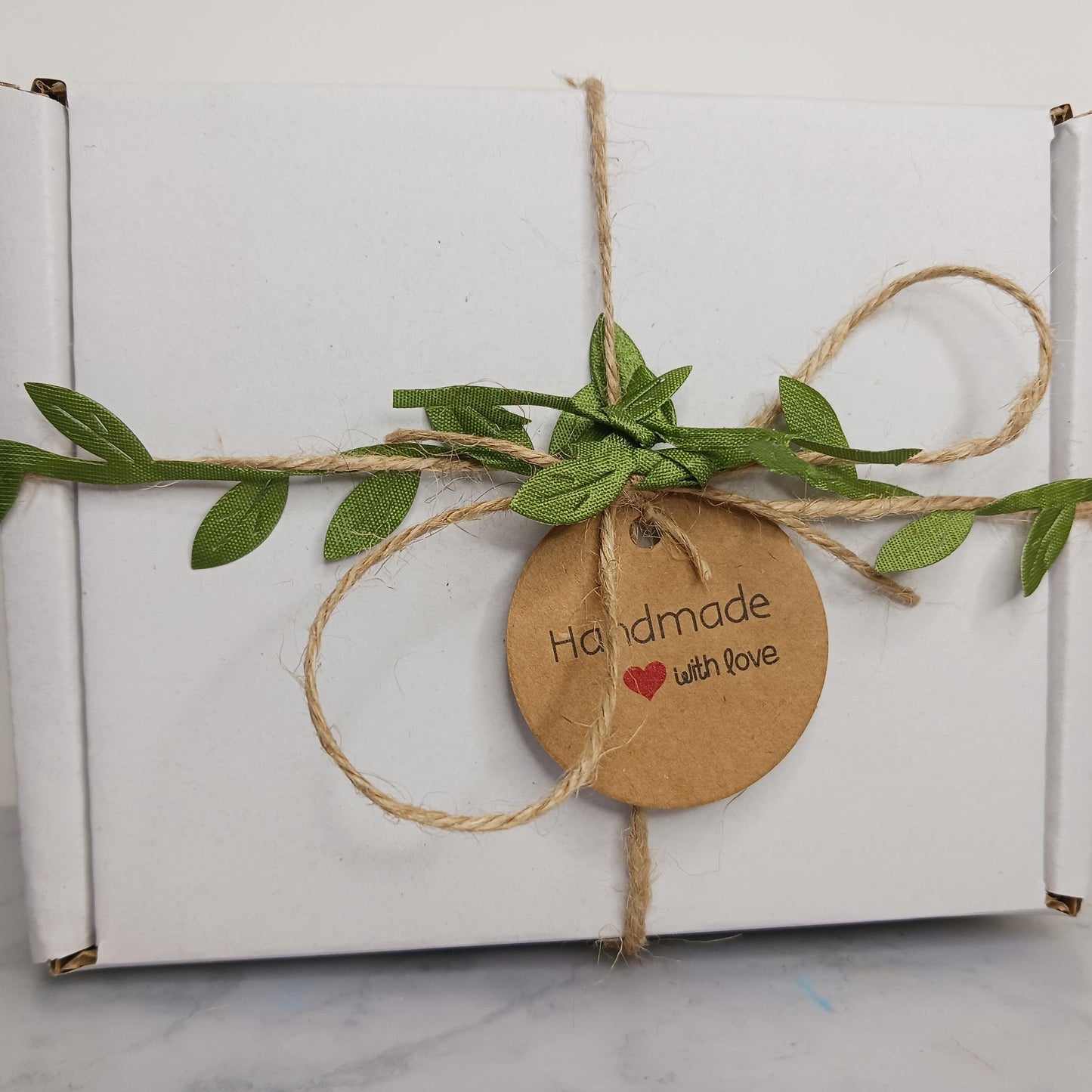 White box wrapped with brown string, green leaves, and a 'Handmade with Love' tag on a white background.