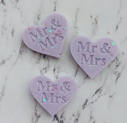 Three heart-shaped 'Mr & Mrs' decorations on a marble surface