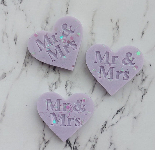 Three heart-shaped 'Mr & Mrs' decorations on a marble surface