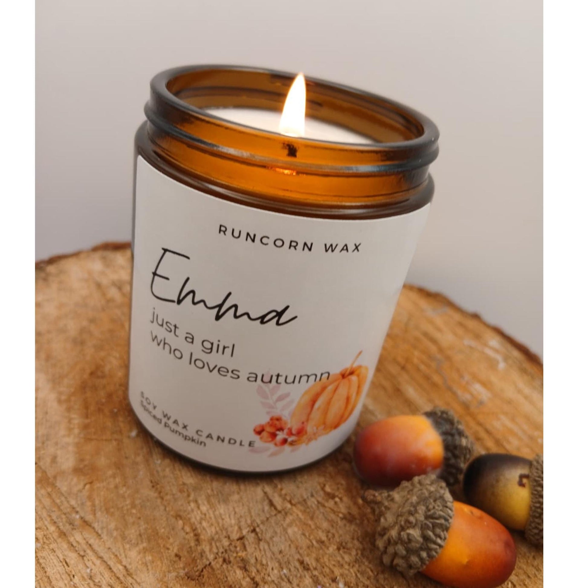 Candle with a label on a wooden surface, surrounded by autumn-themed decorations. pumpkin spice