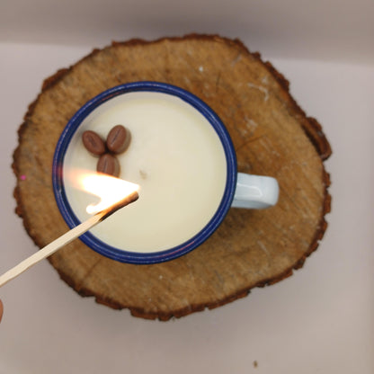 Match being lit near a cup of coffee with two coffee beans on a wooden surface