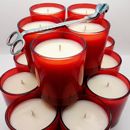 Red candle holders with white candles and a pair of scissors on a white background