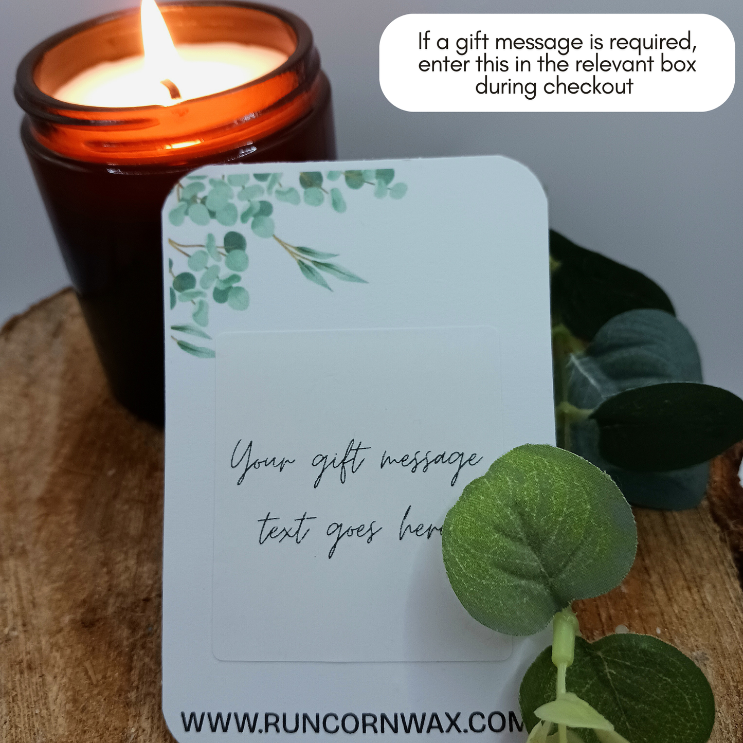 Candle with a decorative card gift message and eucalyptus leaves on a wooden surface