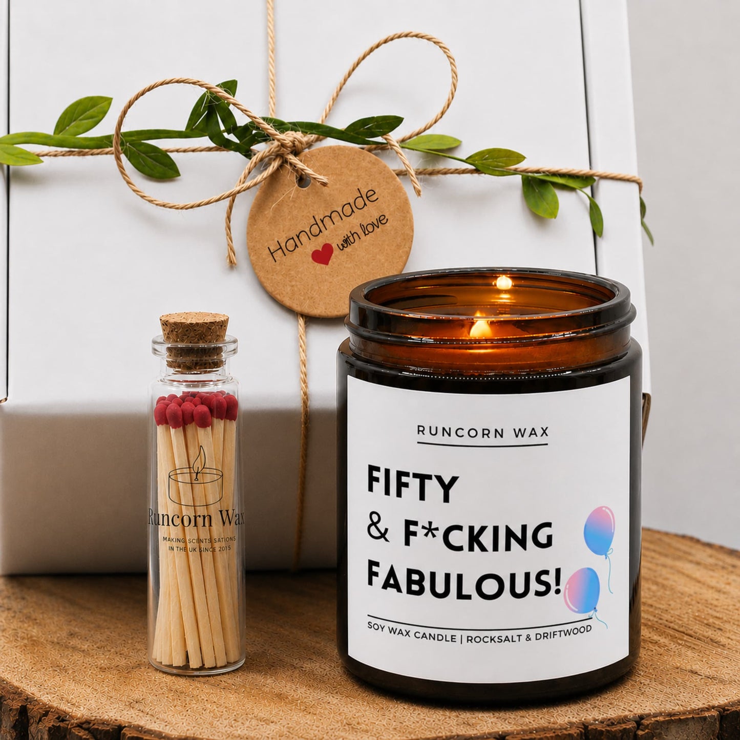 Candle labeled 'Fifty & F*cking Fabulous' with matches and decorative elements on a wooden surface.