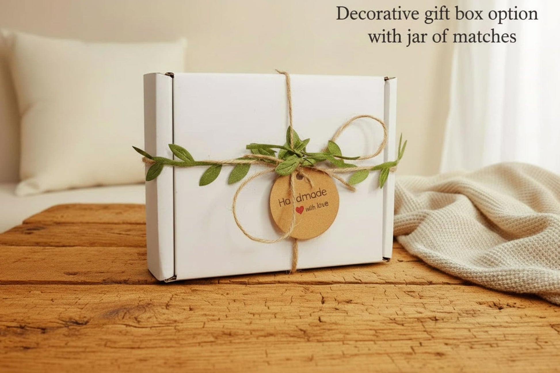 A white box with a brown twine bow and green leaves. The box has a brown tag that says "Handmade with love" with a red heart. The box also has a black and white logo that says "Runcorn Wax" with a candle and hearts.