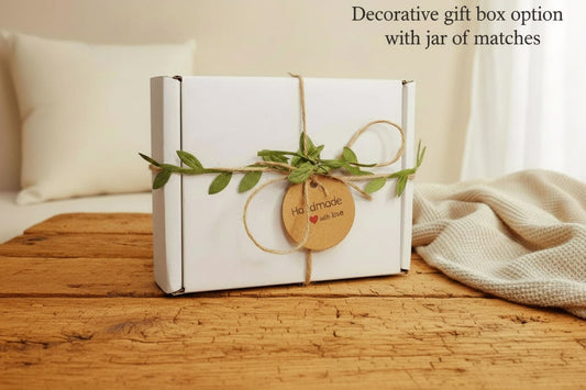 A white box with a brown twine bow and green leaves. The box has a brown tag that says "Handmade with love" with a red heart. The box also has a black and white logo that says "Runcorn Wax" with a candle and hearts.