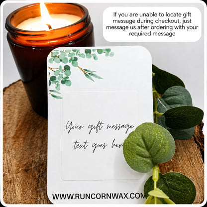 Candle with a decorative card and eucalyptus leaves on a wooden surface, with text overlay. gift message card Candle gift message option display showing card, amber jar candle, and greenery, styled professionally with white border and rounded edges.