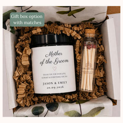 Gift box with 'Mother of the Groom' candle and match bottle on a floral patterned fabric.