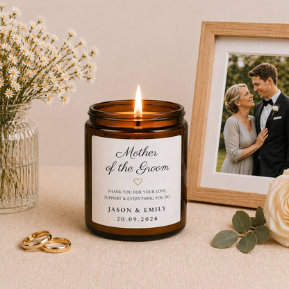 Lit candle in an amber jar with a 'Mother of the Groom' label, surrounded by flowers and a framed photo of mother and groom