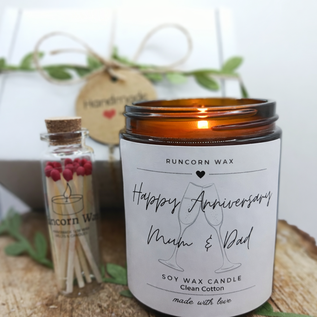 Candle with 'Happy Anniversary Mum & Dad' label and a small bottle of matches on a wooden surface.