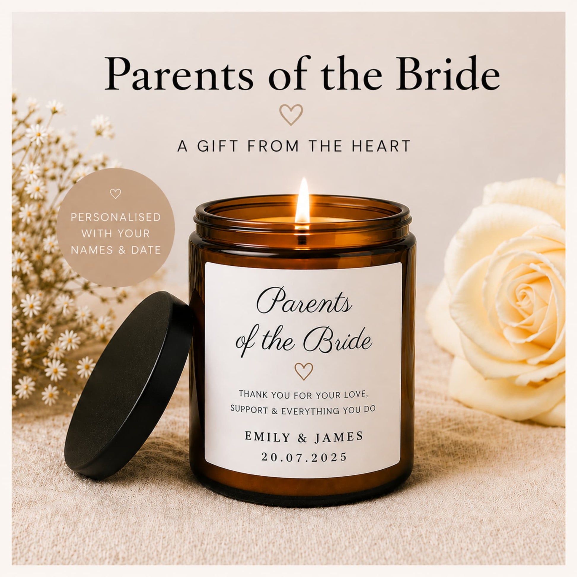 A personalized amber glass jar candle with its black lid resting beside it on a neutral fabric surface. The candle jar has a white label reading 'Parents of the Bride' with a heart and personalized text, and the flame is lit.