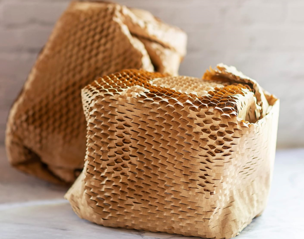 Two honeycomb-shaped honey products wrapped in brown paper on a marble surface.