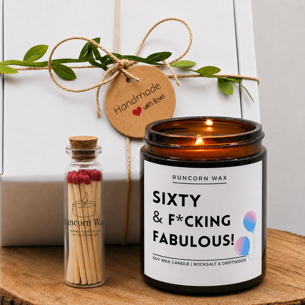 Candle with 'Sixty & F*cking Fabulous!' label and matchbox on a wooden  fifty sixty milestone birthday surface.