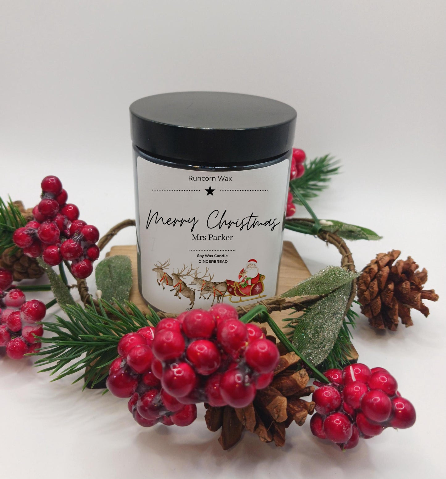 Candle jar with festive design surrounded by red berries and pine cones on a white background