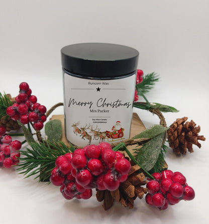 Candle jar with festive design surrounded by red berries and pine cones on a white background