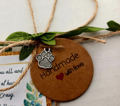 Brown round tag with paw print charm and 'Handmade with Love' text, tied with twine and green leaves.
