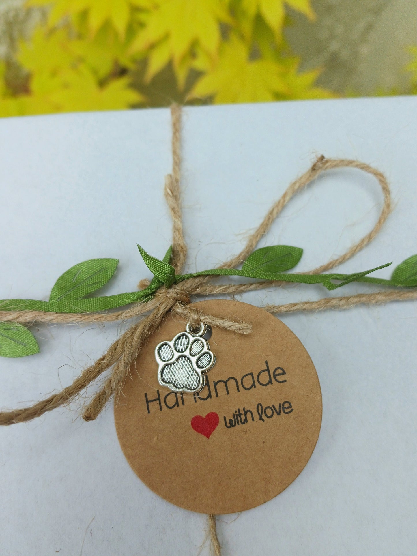 Round brown tag with paw print and text 'Handmade with love' tied with twine and green leaves.