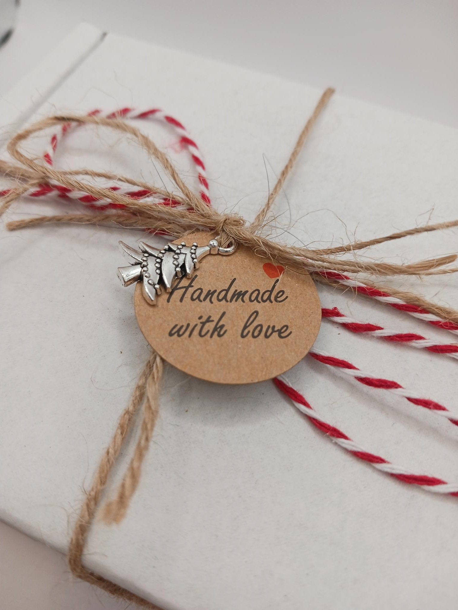Gift wrapped in white paper with red string, brown tag reading 'Handmade with love', and silver charm.