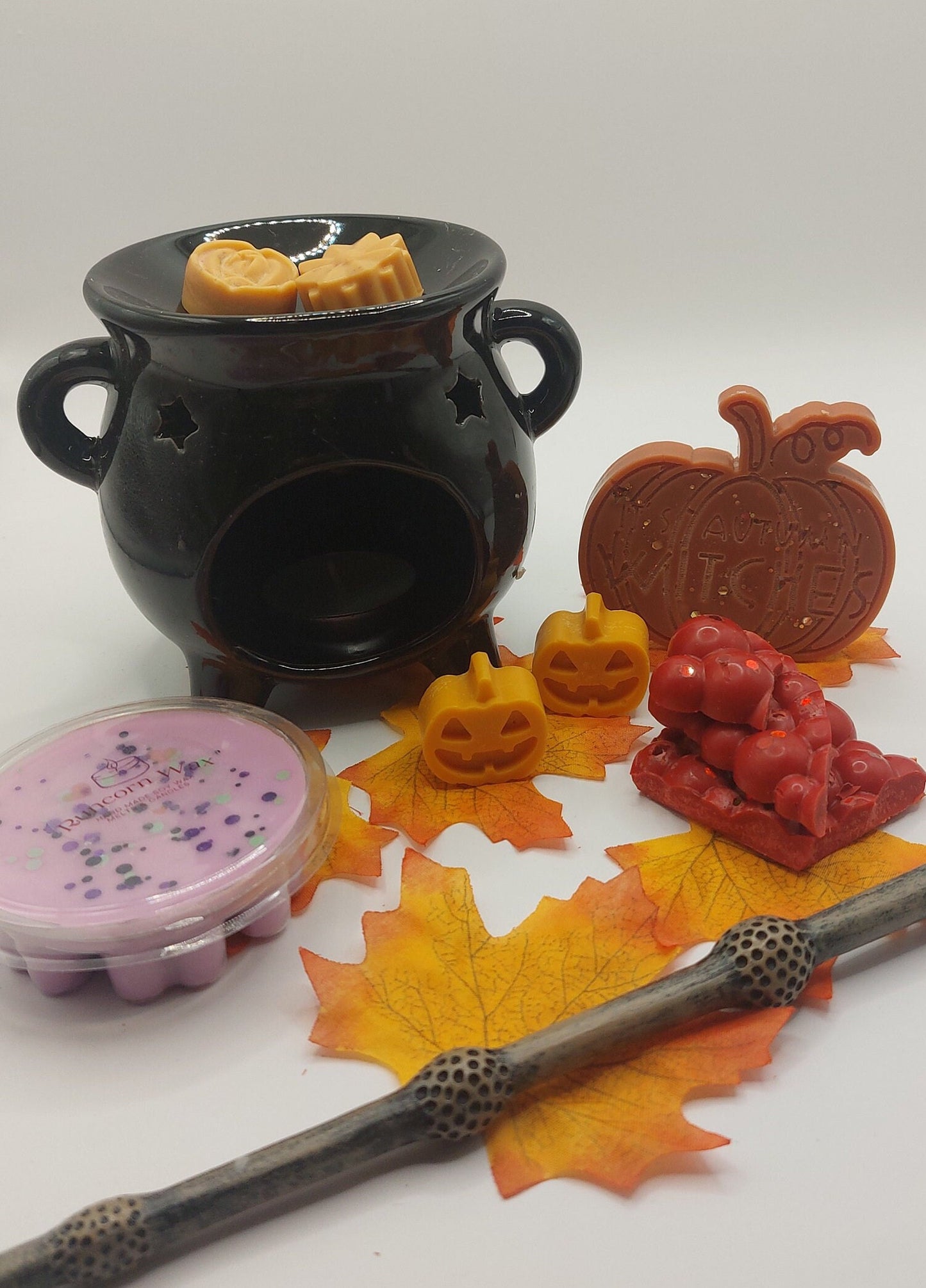 Black ceramic burner with wax melts shaped like pumpkins, a leaf, and a wand on a white background.