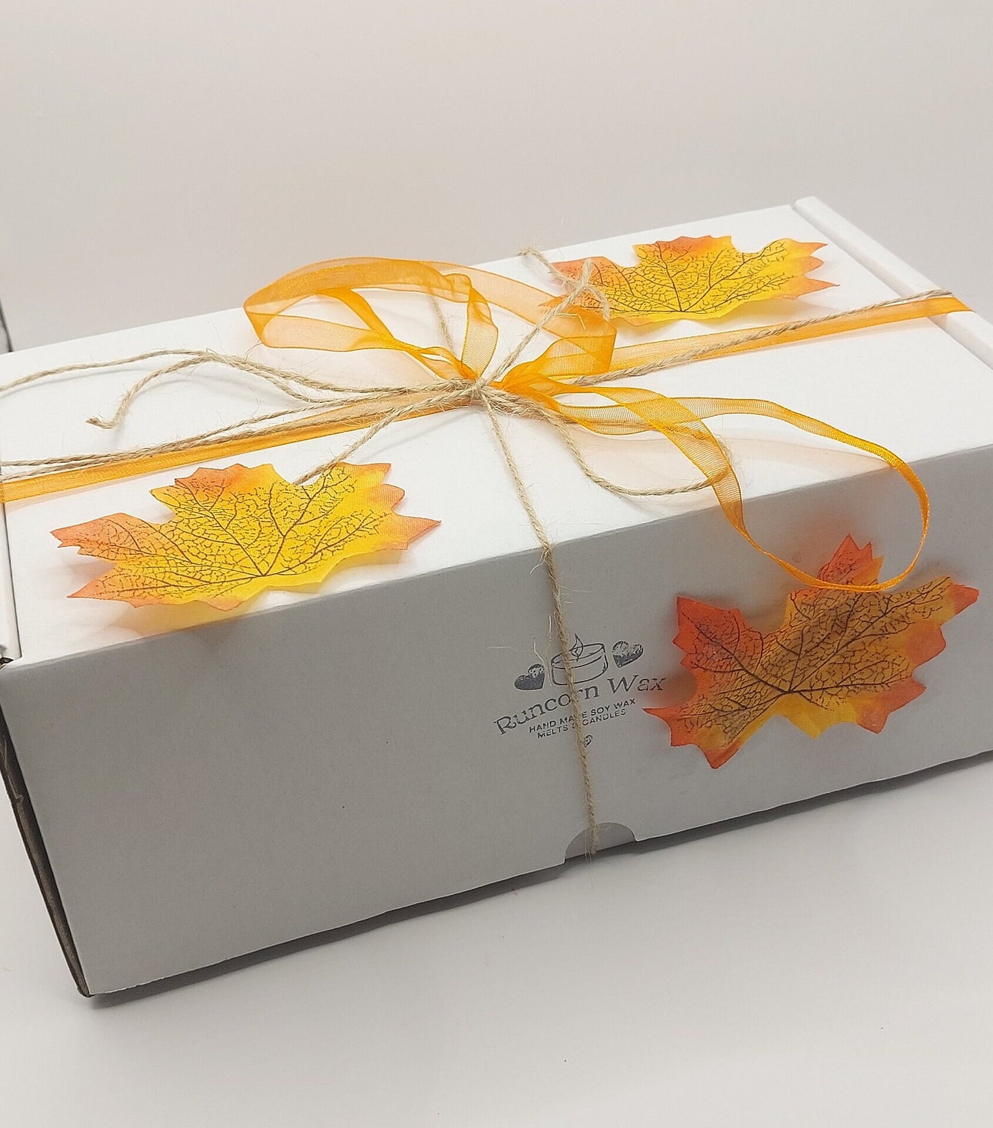 Gift box with autumn leaf decorations and a bow on a white background