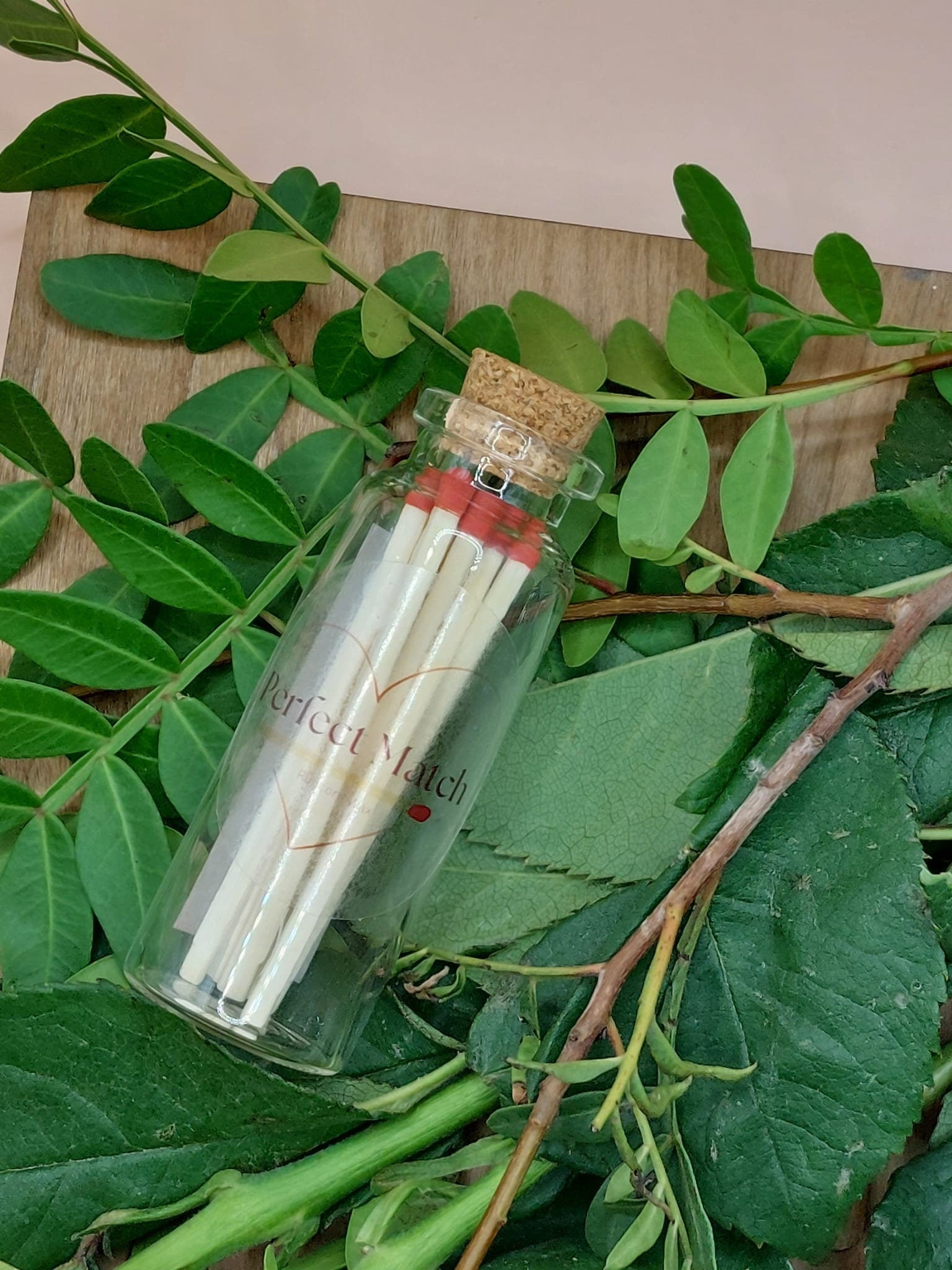 Small glass bottle with matches surrounded by green leaves on a wooden surface