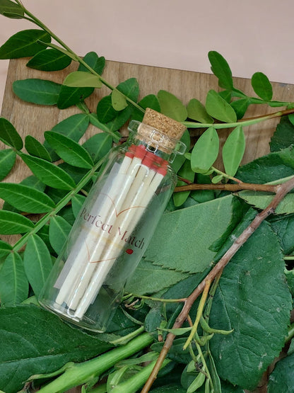 Small glass bottle with matches surrounded by green leaves on a wooden surface