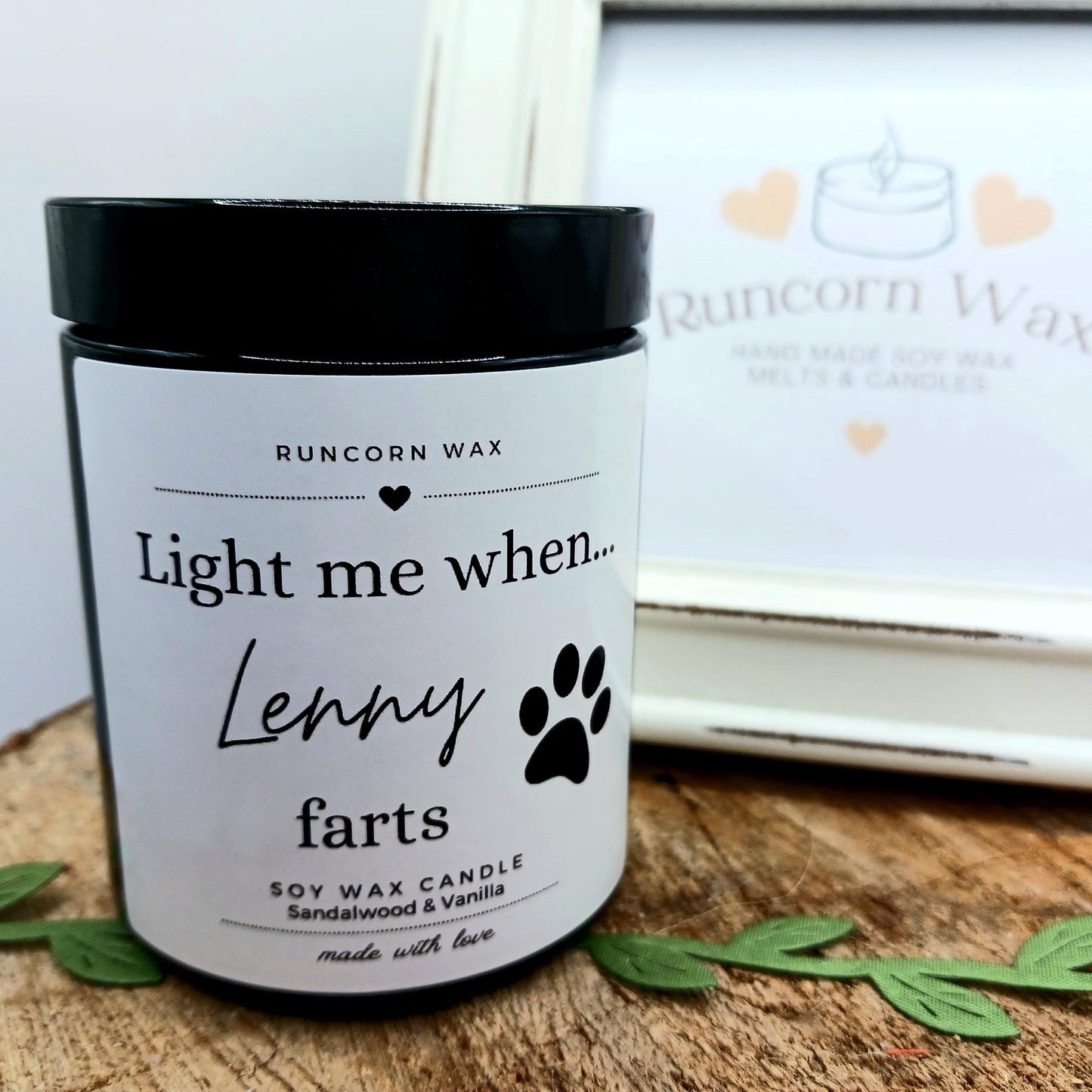 Candle labeled 'Light me when Lenny farts' by Runcorn Wax on a wooden surface.