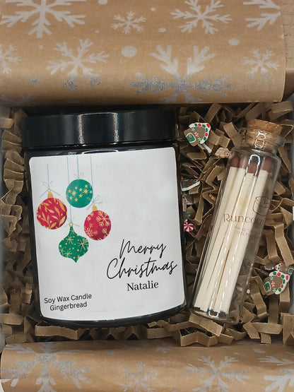 Gift set with a candle labeled 'Merry Christmas Natalie', earrings, and matches on brown paper with snowflake pattern.