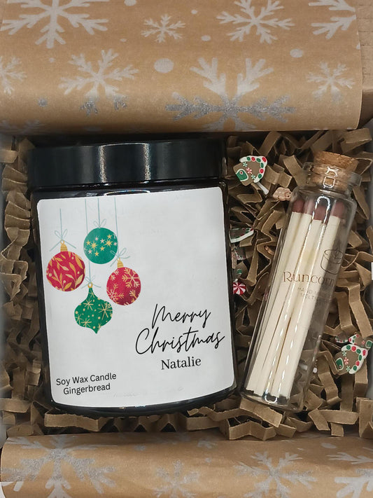 Gift set with a candle labeled 'Merry Christmas Natalie', earrings, and matches on brown paper with snowflake pattern.