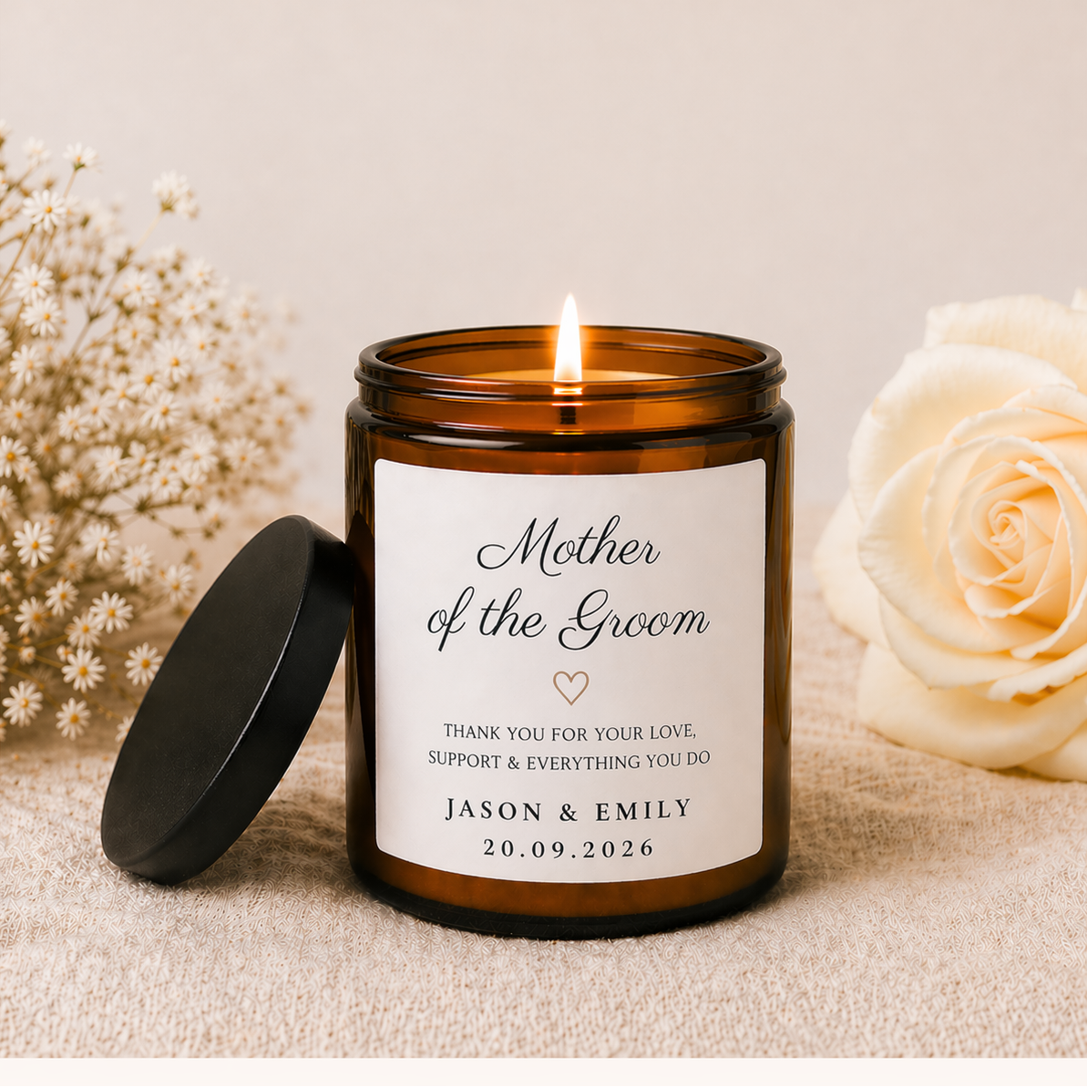 Personalized candle with a label for 'Mother of the Groom' surrounded by flowers on a beige background