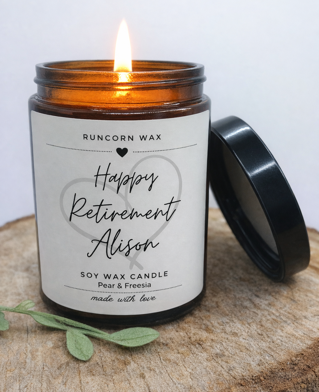 Candle with a personalized label on a wooden surface happy retirement amber candle jar warm lit cosy flame with black urea lid on wooden log.